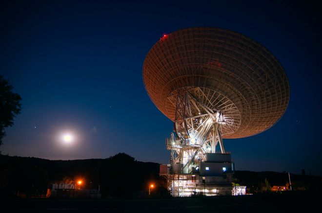 Large parabolic antenna at night representing satellite communication links and RF signal routing